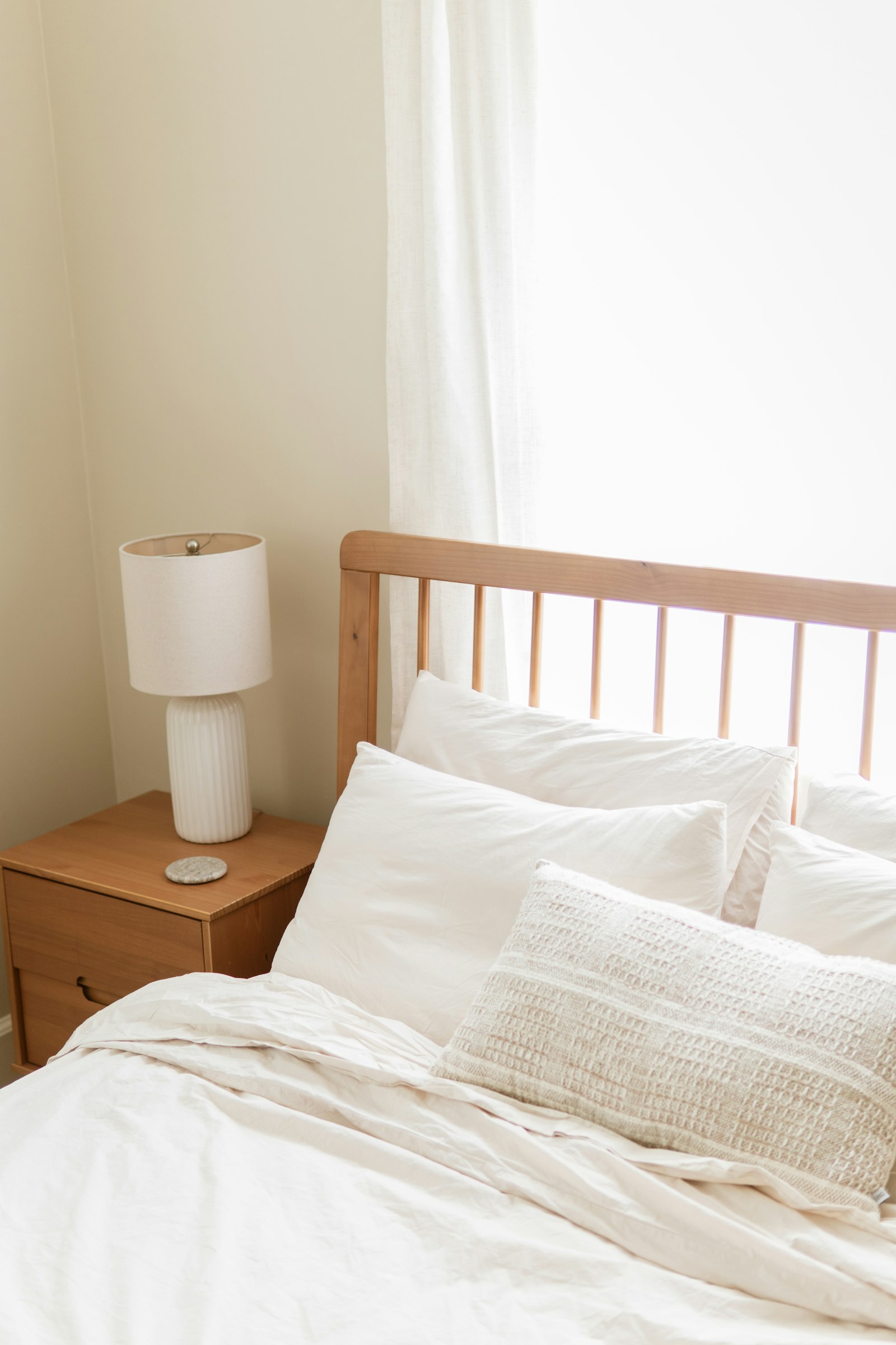 Freshly made bed with white linens, a wooden headboard and a bedside lamp